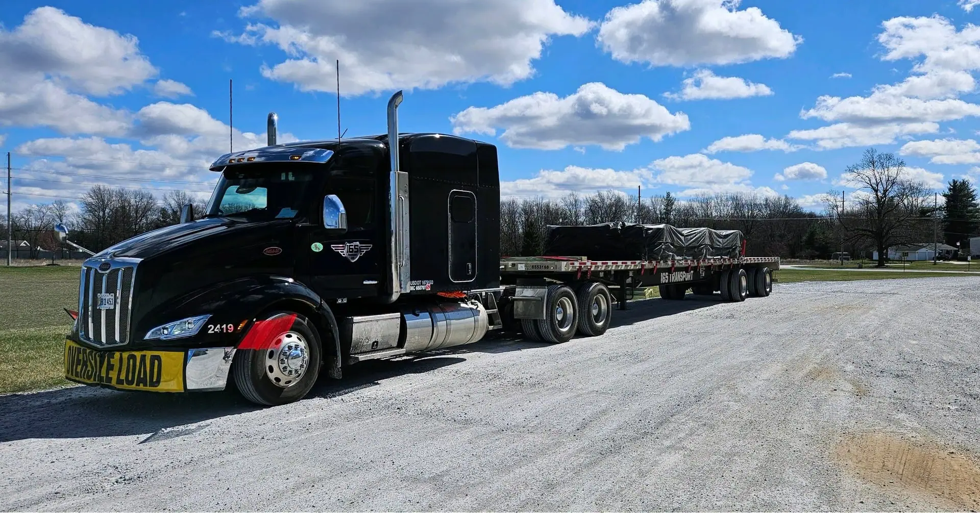 An I65 Transport Peterbilt with an oversize load banner and a tarped flatbed